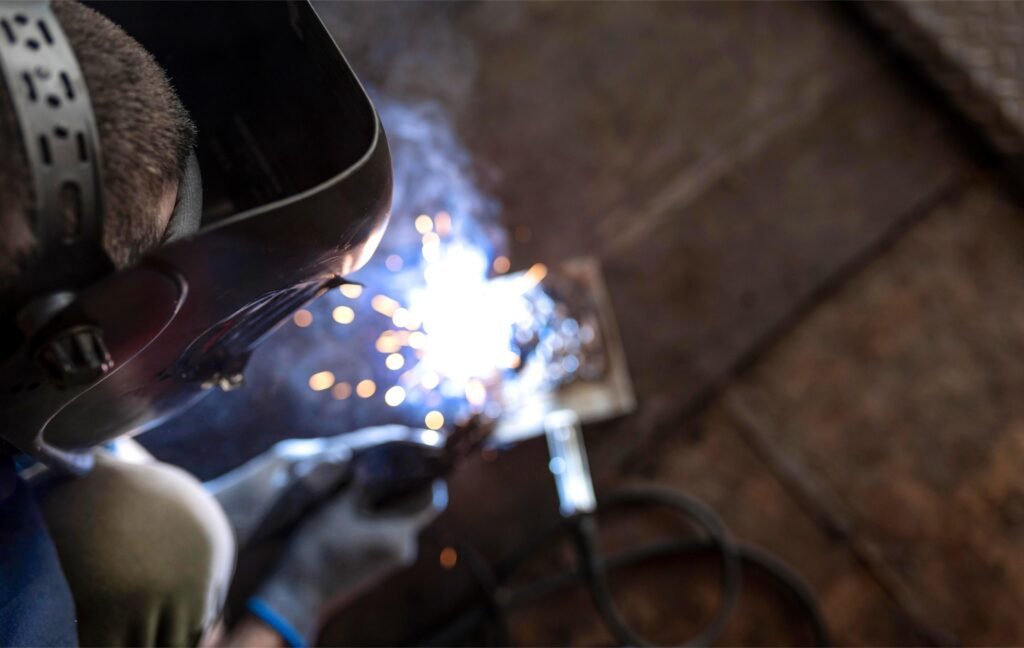 Soudage en cours dans un atelier de tôlerie, avec un soudeur travaillant sur des pièces métalliques sous un éclairage de travail spécialisé.