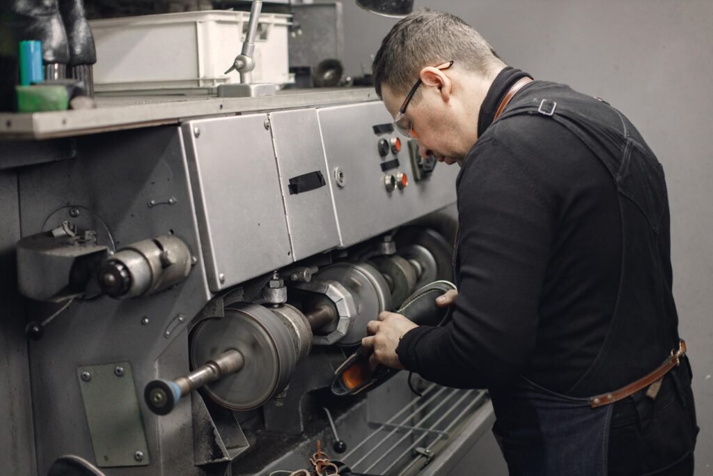 Un artisan expérimenté travaille dans son atelier, portant un tablier et des lunettes de protection, en utilisant une machine spécialisée pour la fabrication de pièces.