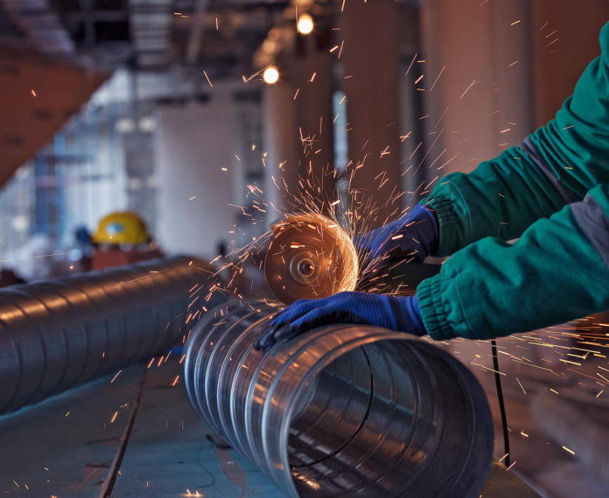 Employé travaillant sur un tuyau de tuyauterie industrielle avec des outils de découpe dans un atelier de chaudronnerie.
