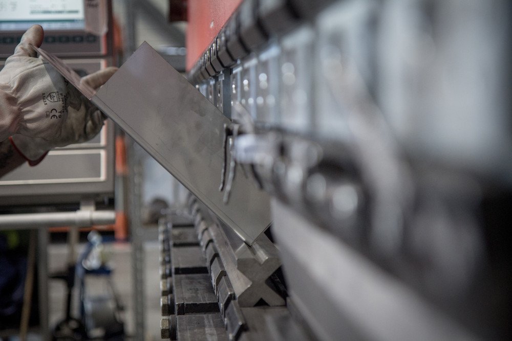 Un travailleur en gants positionne une petite feuille de métal dans une presse plieuse, préparant minutieusement le métal pour un pliage de précision.