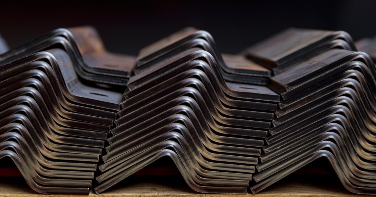 Un complexe industriel de pliage de tôle, montrant des feuilles de métal pliées en formes géométriques complexes, avec un opérateur visible en arrière-plan.