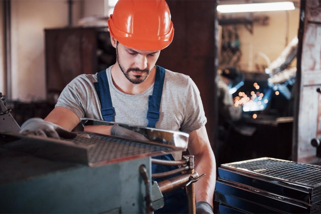 Portrait d'un jeune travailleur portant un casque dans une grande usine de fabrication de pièces métalliques.
